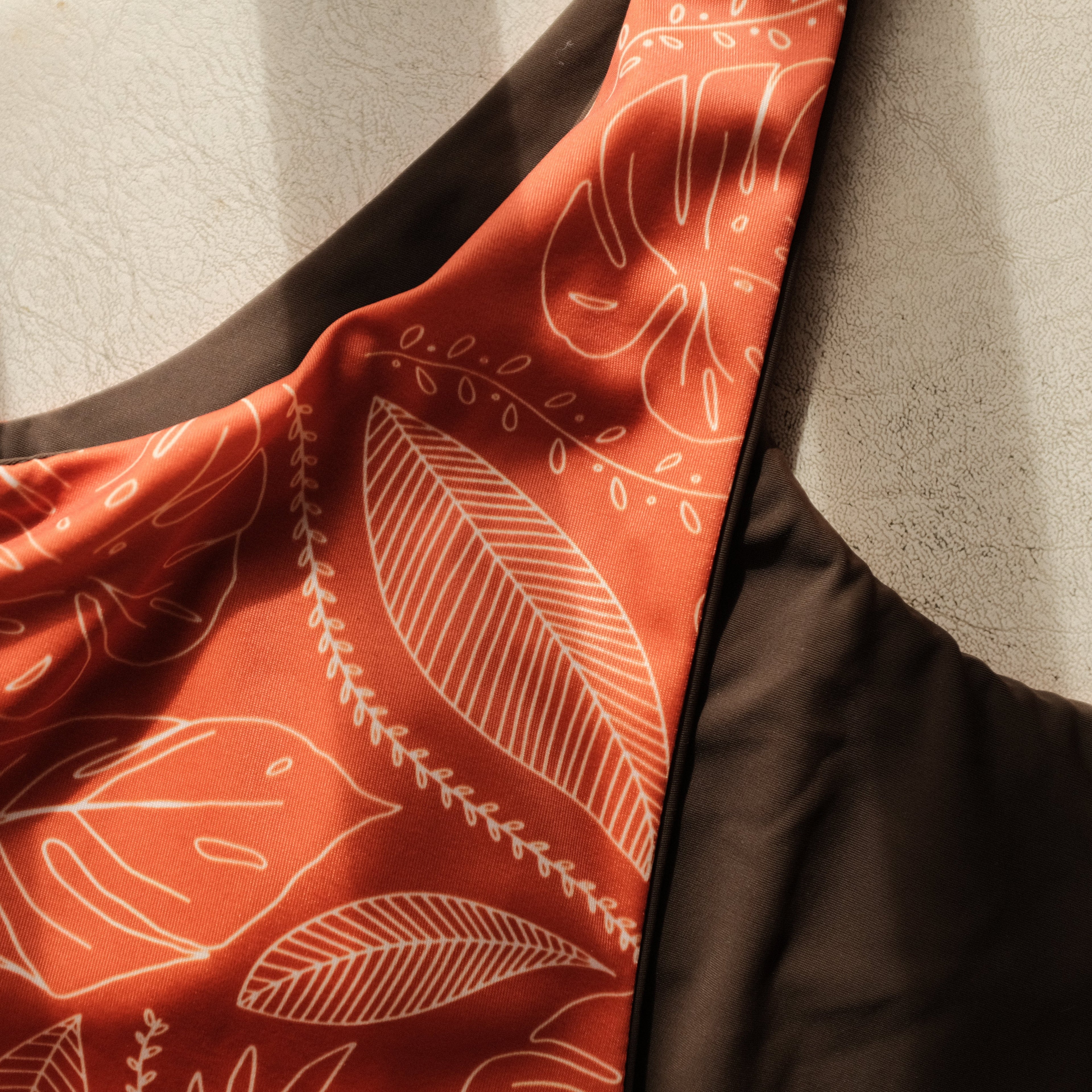 Orange fabric with white leaf pattern draped over a neutral background