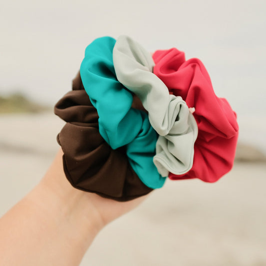 Hand holding four scrunchies in Espresso, ocean, mist and siren colours
